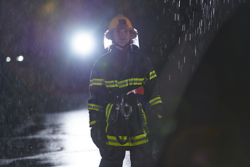 Image showing A determined female firefighter in a professional uniform striding through the dangerous, rainy night on a daring rescue mission, showcasing her unwavering bravery and commitment to saving lives.