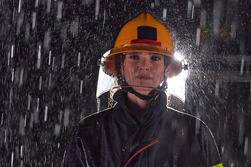 Image showing A determined female firefighter in a professional uniform striding through the dangerous, rainy night on a daring rescue mission, showcasing her unwavering bravery and commitment to saving lives.