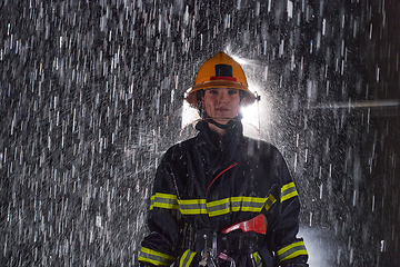 Image showing A determined female firefighter in a professional uniform striding through the dangerous, rainy night on a daring rescue mission, showcasing her unwavering bravery and commitment to saving lives.