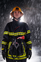 Image showing A determined female firefighter in a professional uniform striding through the dangerous, rainy night on a daring rescue mission, showcasing her unwavering bravery and commitment to saving lives.