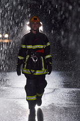 Image showing A determined female firefighter in a professional uniform striding through the dangerous, rainy night on a daring rescue mission, showcasing her unwavering bravery and commitment to saving lives.