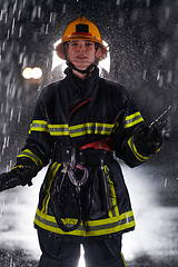 Image showing A determined female firefighter in a professional uniform striding through the dangerous, rainy night on a daring rescue mission, showcasing her unwavering bravery and commitment to saving lives.