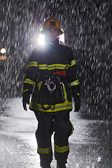 Image showing A determined female firefighter in a professional uniform striding through the dangerous, rainy night on a daring rescue mission, showcasing her unwavering bravery and commitment to saving lives.