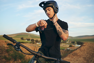 Image showing Sports, bike and man checking his pulse on a mountain dirt road in nature for race or competition training. Fitness, exercise and young male biker athlete with watch for the time at an outdoor trail.