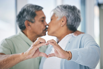 Image showing Heart hands, mature couple and kiss with love, kindness and commitment to partner at home. Man, woman and finger shape for sign of support, trust and care of icon of emoji, loyalty and retirement