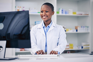 Image showing Pharmacist, typing and happy black woman on computer in pharmacy, drugstore or shop. Smile, medical professional and African doctor on internet for telehealth, healthcare and research for medicine.