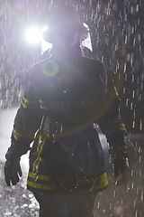 Image showing A determined female firefighter in a professional uniform striding through the dangerous, rainy night on a daring rescue mission, showcasing her unwavering bravery and commitment to saving lives.