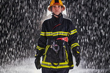 Image showing A determined female firefighter in a professional uniform striding through the dangerous, rainy night on a daring rescue mission, showcasing her unwavering bravery and commitment to saving lives.