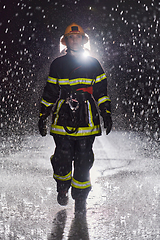 Image showing A determined female firefighter in a professional uniform striding through the dangerous, rainy night on a daring rescue mission, showcasing her unwavering bravery and commitment to saving lives.