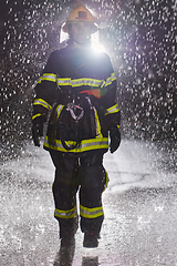 Image showing A determined female firefighter in a professional uniform striding through the dangerous, rainy night on a daring rescue mission, showcasing her unwavering bravery and commitment to saving lives.