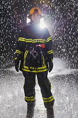 Image showing A determined female firefighter in a professional uniform striding through the dangerous, rainy night on a daring rescue mission, showcasing her unwavering bravery and commitment to saving lives.