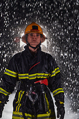 Image showing A determined female firefighter in a professional uniform striding through the dangerous, rainy night on a daring rescue mission, showcasing her unwavering bravery and commitment to saving lives.