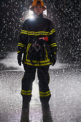 Image showing A determined female firefighter in a professional uniform striding through the dangerous, rainy night on a daring rescue mission, showcasing her unwavering bravery and commitment to saving lives.