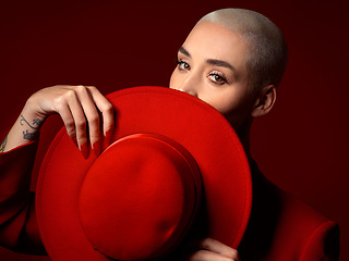 Image showing Portrait, fashion and hat with a woman on a red background in studio for elegant or trendy style. Face, hide and cover with a young female model looking edgy or classy in a suit or unique clothes