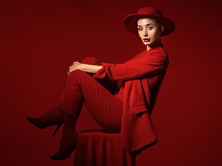 Image showing Portrait, fashion and a woman on a chair in studio on a red background for elegant or trendy style. Aesthetic, art and beauty with a young female person sitting in an edgy, classy or unique suit