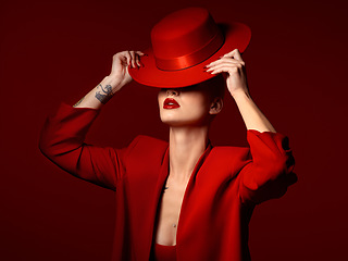 Image showing Woman, red aesthetic and hat in studio with makeup art, thinking and mystery with couture, vision and background. Girl, model and high fashion with suit, mindset and facial paint for cosmetic beauty