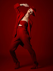 Image showing Catwalk, fashion and a woman on red background in studio for elegant or trendy style. Aesthetic, art and beauty with a young female runway model posing in an edgy or classy suit for a magazine cover