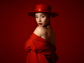 Image showing Portrait, fashion and shoulder with a woman on a red studio background for elegant or trendy style. Aesthetic beauty, art and hat with a young female model looking edgy or classy in a unique outfit