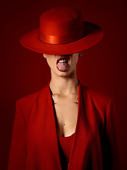 Image showing Woman, red aesthetic and beauty with hat, makeup art and tongue out for couture, emoji and studio background. Girl, model and high fashion with suit, mindset and sexy with lipstick for cosmetics