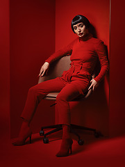 Image showing Chair, fashion and a model woman on red background in studio for elegant, chic or trendy style. Aesthetic, art and confident beauty with an edgy or classy young person in a unique clothes or suit