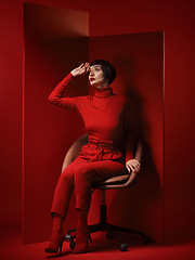 Image showing Thinking, fashion and a model woman on red background in studio for elegant, chic or trendy style. Aesthetic, art and beauty with an edgy person in unique clothes suit, makeup and cosmetics on chair