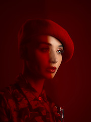 Image showing Woman, fashion and face with red aesthetic, beauty and makeup with vintage hat isolated on studio background. Retro style, female model with serious expression and cosmetics, attractive and bold