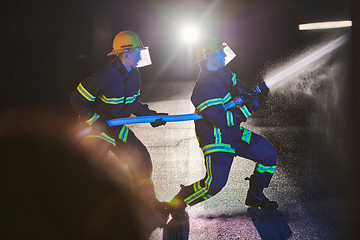 Image showing Firefighters using a water hose to eliminate a fire hazard. Team of female and male firemen in dangerous rescue mission.