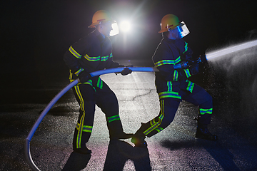 Image showing Firefighters using a water hose to eliminate a fire hazard. Team of female and male firemen in dangerous rescue mission.