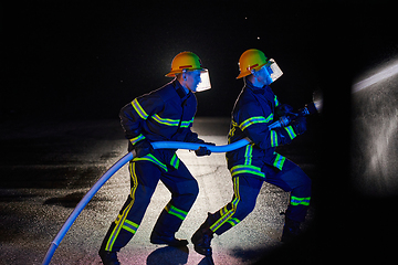 Image showing Firefighters using a water hose to eliminate a fire hazard. Team of female and male firemen in dangerous rescue mission.