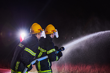 Image showing Firefighters using a water hose to eliminate a fire hazard. Team of female and male firemen in dangerous rescue mission.