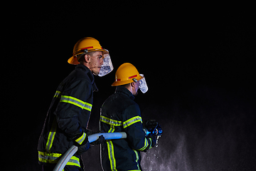 Image showing Firefighters using a water hose to eliminate a fire hazard. Team of female and male firemen in dangerous rescue mission.