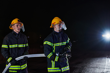 Image showing Firefighters using a water hose to eliminate a fire hazard. Team of female and male firemen in dangerous rescue mission.