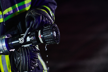 Image showing Firefighter using a water hose to eliminate a fire hazard. Team of firemen in the dangerous rescue mission.