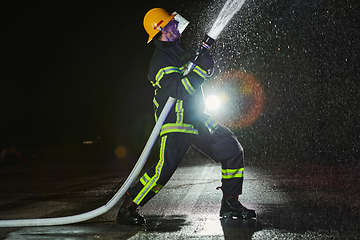 Image showing Firefighter using a water hose to eliminate a fire hazard. Team of firemen in the dangerous rescue mission.