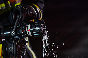 Image showing Firefighter using a water hose to eliminate a fire hazard. Team of firemen in the dangerous rescue mission.