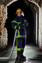 Image showing Firefighter using a water hose to eliminate a fire hazard. Team of female and male firemen in dangerous rescue mission.