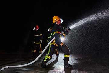 Image showing Firefighters using a water hose to eliminate a fire hazard. Team of female and male firemen in dangerous rescue mission.