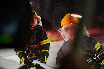 Image showing Firefighters using a water hose to eliminate a fire hazard. Team of female and male firemen in dangerous rescue mission.