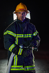 Image showing Firefighter using a water hose to eliminate a fire hazard. Team of female and male firemen in dangerous rescue mission.