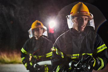 Image showing Firefighters using a water hose to eliminate a fire hazard. Team of female and male firemen in dangerous rescue mission.