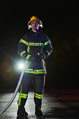 Image showing Firefighters using a water hose to eliminate a fire hazard. Team of female and male firemen in dangerous rescue mission.