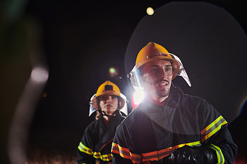 Image showing Firefighters using a water hose to eliminate a fire hazard. Team of female and male firemen in dangerous rescue mission.