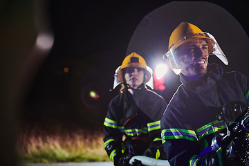 Image showing Firefighters using a water hose to eliminate a fire hazard. Team of female and male firemen in dangerous rescue mission.