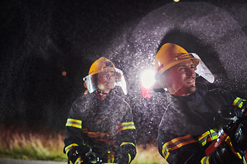 Image showing Firefighters using a water hose to eliminate a fire hazard. Team of female and male firemen in dangerous rescue mission.