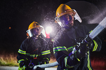 Image showing Firefighters using a water hose to eliminate a fire hazard. Team of female and male firemen in dangerous rescue mission.