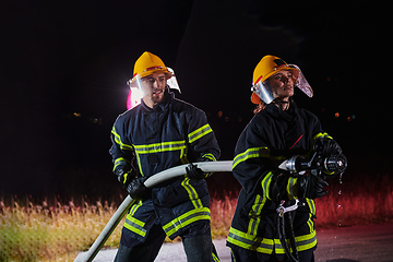 Image showing Firefighters using a water hose to eliminate a fire hazard. Team of female and male firemen in dangerous rescue mission.