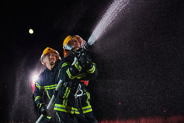 Image showing Firefighters using a water hose to eliminate a fire hazard. Team of female and male firemen in dangerous rescue mission.