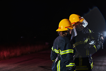 Image showing Firefighters using a water hose to eliminate a fire hazard. Team of female and male firemen in dangerous rescue mission.