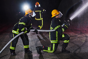 Image showing Firefighters using a water hose to eliminate a fire hazard. Team of female and male firemen in dangerous rescue mission.