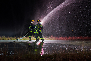 Image showing Firefighters using a water hose to eliminate a fire hazard. Team of female and male firemen in dangerous rescue mission.